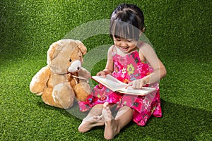 Asian Chinese little girl reading book with teddy bear