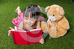 Asian Chinese little girl reading book with teddy bear