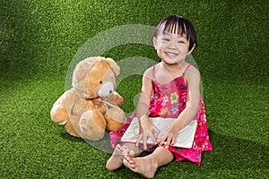 Asian Chinese little girl reading book with teddy bear