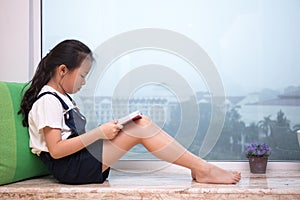 Asian Chinese little girl reading book on the windowsill