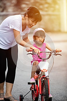 Asian Chinese little girl riding bicycle with mom guide