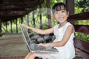 Asian Chinese little girl sitting on the bench with laptop