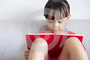 Asian Chinese little girl sitting on the sofa reading book