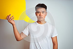 Asian chinese man holding speech bubble standing over isolated white background with a confident expression on smart face thinking