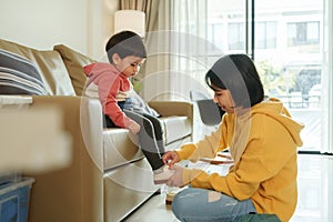 Asian Chinese mother helping her son put shoes on