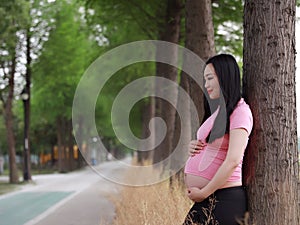 Asian Chinese pregnant woman in yoga dress lean on tree relaxed joyful peaceful life fresh air forest outdoor
