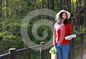 Asian Chinese pretty woman hold a book and flowers wear a hat in nature in spring outdoor