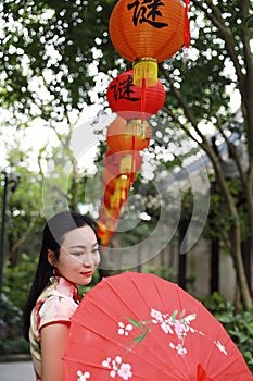 Asian Chinese woman artist traditional chi-pao cheongsam in a garden hold red parasol lantern on Mid-autumn Festival holiday