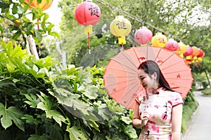 Asian Chinese woman artist traditional chi-pao cheongsam in a garden hold red parasol lantern on Mid-autumn Festival holiday