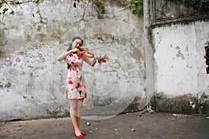 Asian Chinese woman artist in traditional chi-pao cheongsam in a garden play musical instruments violin ancient historic building