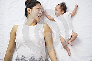Asian chinese woman mother lying next to newborn child and playing