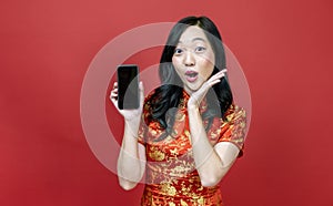 Asian chinese woman with red cheongsam or qipao holding mobile phone for Chinese New Year celebration holiday isolated on red
