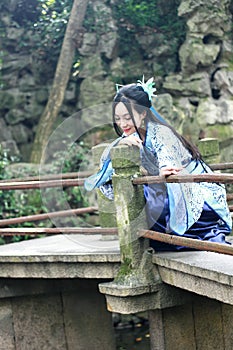 Asian Chinese woman in traditional Blue and white Hanfu dress, play in a famous garden Climb on the bent bridge