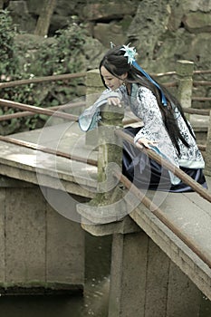 Asian Chinese woman in traditional Blue and white Hanfu dress, play in a famous garden Climb on the bent bridge