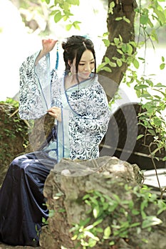 Asian Chinese woman in traditional Blue and white Hanfu dress, play in a famous garden ,sit on an ancient stone chair