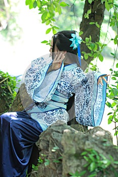 Asian Chinese woman in traditional Blue and white Hanfu dress, play in a famous garden ,sit on an ancient stone chair