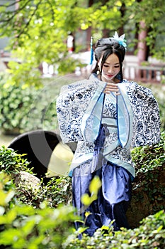 Asian Chinese woman in traditional Blue and white Hanfu dress, play in a famous garden ,sit on an ancient stone chair