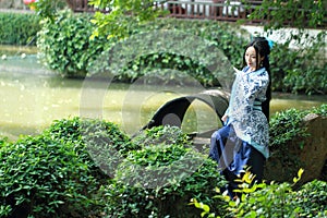 Asian Chinese woman in traditional Blue and white Hanfu dress, play in a famous garden ,sit on an ancient stone chair