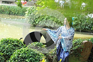 Asian Chinese woman in traditional Blue and white Hanfu dress, play in a famous garden ,sit on an ancient stone chair