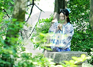 Asian Chinese woman in traditional Blue and white Hanfu dress, play in a famous garden ,sit on an ancient stone chair