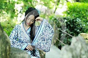 Asian Chinese woman in traditional Blue and white Hanfu dress, play in a famous garden ,sit on an ancient stone chair