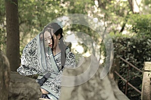 Asian Chinese woman in traditional Blue and white Hanfu dress, play in a famous garden ,sit on an ancient stone chair