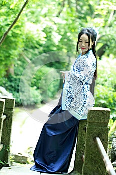 Asian Chinese woman in traditional Blue and white Hanfu dress, play in a famous garden ,Sit on the bridge