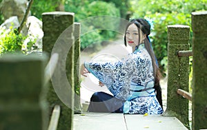 Asian Chinese woman in traditional Blue and white Hanfu dress, play in a famous garden ,Sit on the bridge