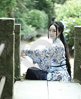 Asian Chinese woman in traditional Blue and white Hanfu dress, play in a famous garden ,Sit on the bridge