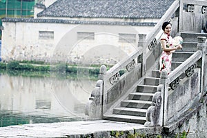 Asian Chinese woman in traditional cheongsam stand on a ancient bridge photo