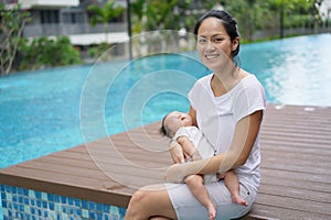 Asian chinese young mother carrying newborn child at her home swimming pool