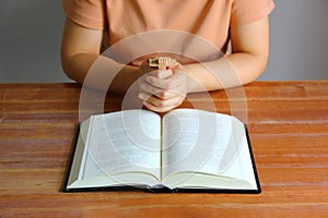 Asian Christain woman praying while holding wood cross in front of the bible