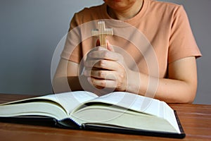 Asian Christain woman praying while holding wood cross in front of the bible