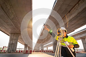 Asian civil engineer or surveyor making measuring and pointing finger under the expressway with theodolite on road works. Survey