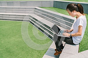 Asian college student or freelance woman using laptop on stair in university campus or public park. Information technology concept