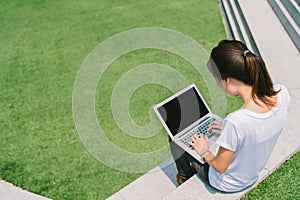 Asian college student or freelance woman using laptop on stairs in university campus or modern park