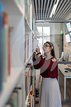 Asian college student in library. Concentrated girl picking books to prepare for exam in university