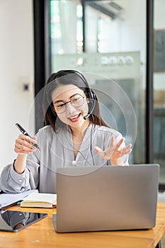 Asian college student wears wireless headphones and writes on a laptop to learn languages online Watch and listen to speakers` Lap