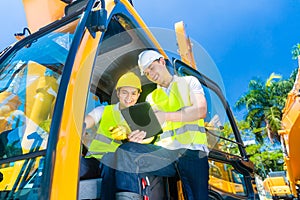 Asian construction driver discussing with engineer blueprints