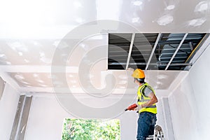 Asian construction worker assemble a suspended ceiling with drywall and fixing the drywall to the ceiling metal frame with