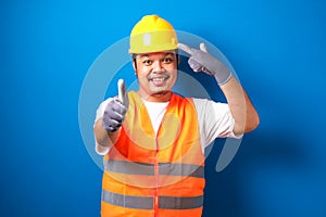 Asian construction worker man wearing orange safety vest and helmet pointing to head with his finger