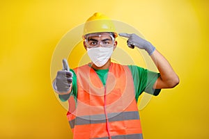 Asian construction worker pointing at his protective mask and savety helmet