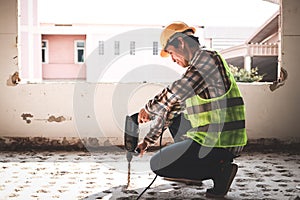 Asian construction worker using mortar extraction machine to drill concrete floor.