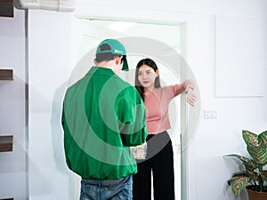 Asian consumer woman hungry and show wrist watch to delivery man who wearing green uniform with jacket and cap because send order