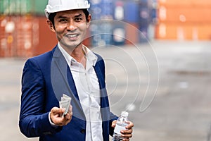 The Asian container yard manager holds cash and a water bottle in hand. With a smiling face