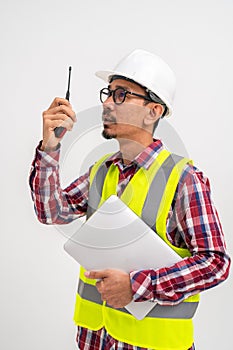 Asian contractor in helmet wearing vest is using walkie talkie with laptop standing on white background. Construction contractor
