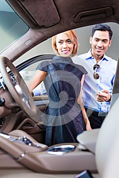 Asian couple choosing luxury car in dealership