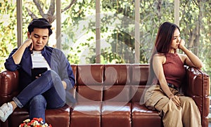 Asian couple got upset,man and woman sitting on the other side of sofa in living room , no talking ,no smiling , having some