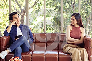 Asian couple got upsetting ,man and woman sitting on the other side of sofa in living room , looking to each other .no talking ,no