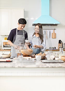 Asian couple Help each other to make a bakery In a romantic atmosphere in the kitchen at home. Young people work together to mix